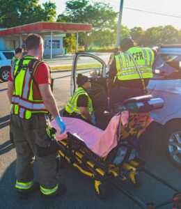 Polk County Fire Rescue paramedics prepare to assist a patient inside a vehicle at the scene of a traffic crash. An ambulance stretcher is positioned beside the car as emergency responders work together to provide care.